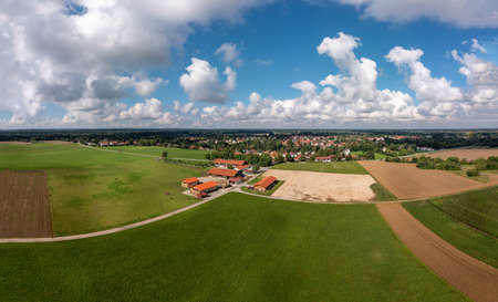 Aerial view over a ranch with horses and a village in the background under a blue, wonderful fluffy clouded sky.の写真素材