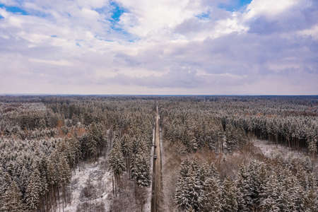 Idyllic winter panorama from an aerial view with a snow-covered forest and a to the horizon leading road.の写真素材
