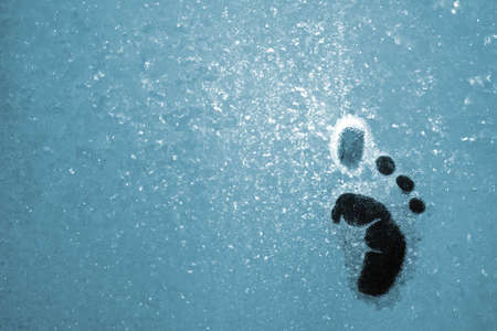 small humanoid foot step on blue icy window glassの写真素材
