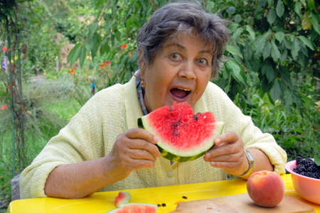 senior woman eating watermelon with join in thre gardenの写真素材