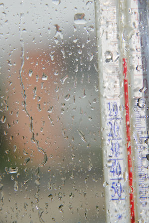 rainy autumn began outside window, drops on the glass and street thermometer