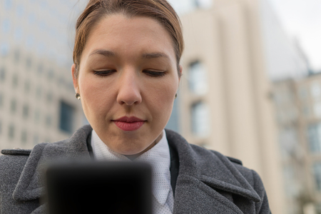 Stressed business woman holding cellphone in hands on the city streetの写真素材