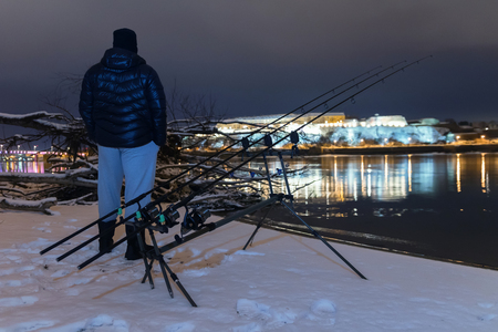Night Fishing Fisherman in Winter night. Night Fishing, Winter fishing. Carp Rods, Night reflection. City lights.の写真素材