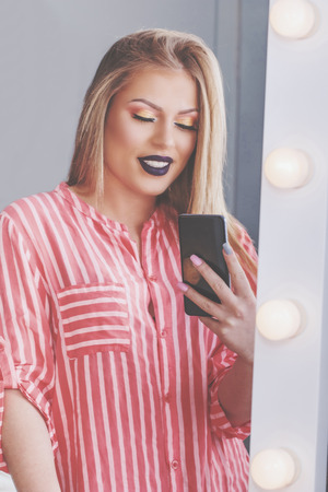 Attractive blonde girl makes selfie in makeup mirror with lampsの写真素材