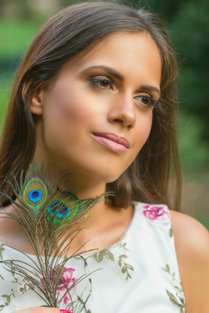 Portrait of young woman holding peacock feather outdoor.の写真素材