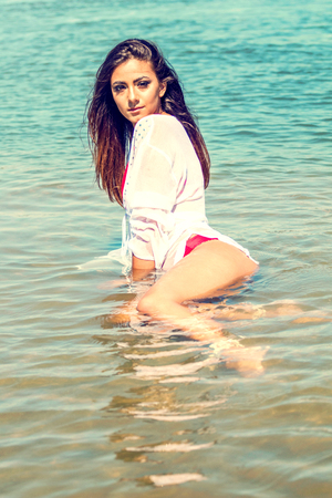 Beautiful brunette Caucasian woman relaxing in shallow water Fashion portrait Summer time Sunny dayの写真素材