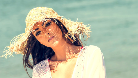 Portrait of beautiful young woman wearing summer hat at beach. Closeup Portrait girl with straw hatの写真素材
