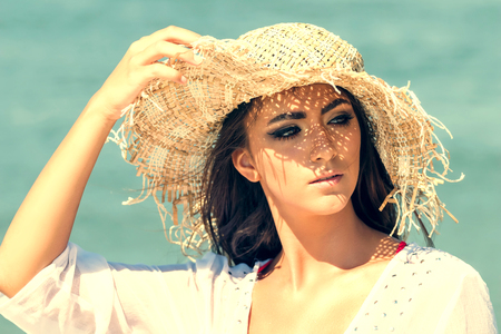Portrait of beautiful young woman wearing summer hat at beach. Closeup Portrait girl with straw hatの写真素材