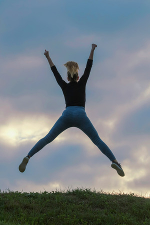 Cheerful Positive Girl Jumping in the Air Outdoor Morning Clouds, Athlete Woman Jump Beautiful Sunrise Morning Workoutの写真素材