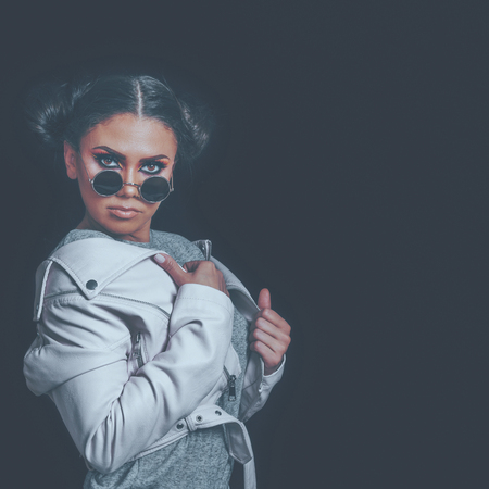 Fashion Girl Posing, wearing Urban Hipster Style, Sweet Pastel Colors, Trendy Sunglasses, Pink Jacket, Dark Background.の写真素材