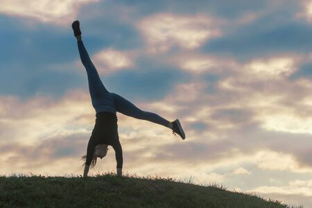 Young woman doing cartwheel on the grass Morning workout beautiful sunriseの写真素材
