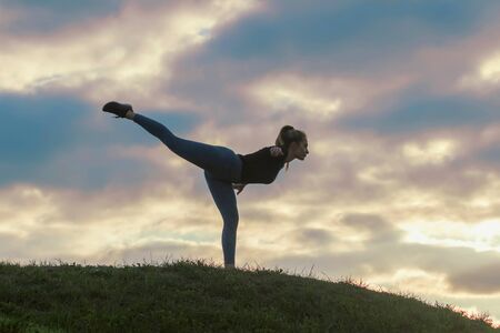 Young Woman Standing On One Leg And Exercising On the Grass Morning Workout, Beautiful Sunriseの写真素材