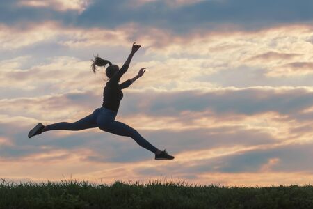 Sporty young woman jumping outdoor morning clouds background, Athlete Woman jump beautiful sunrise morning workoutの写真素材