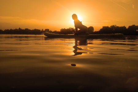 Woman on sup board, paddle boarding at sunset reflection on water