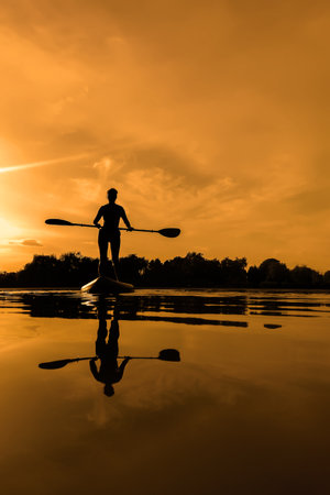 Woman on sup board, paddle boarding at sunset reflection on waterの写真素材
