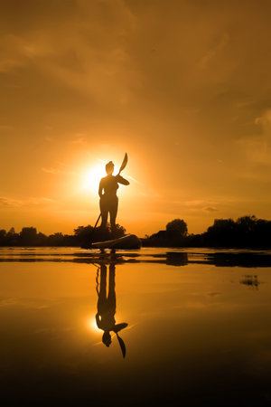 Woman on sup board, paddle boarding at sunset reflection on waterの写真素材