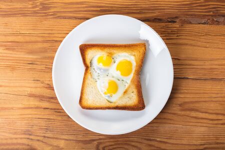 fried quail eggs in a toast on wooden background