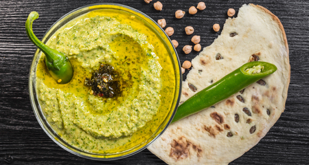 Hummus with spinach and hot pepper on a black wooden background