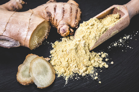 spices ginger in a wooden scoop on black backgroundの写真素材