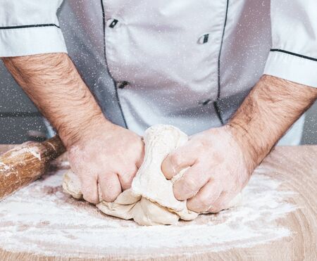 male cook kneads dough on the table, hands close-up