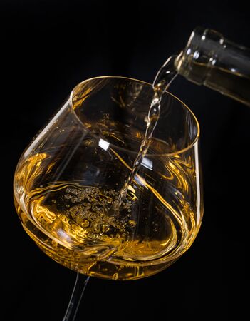 white wine pouring from bottle into a wineglass on black backgroundの写真素材