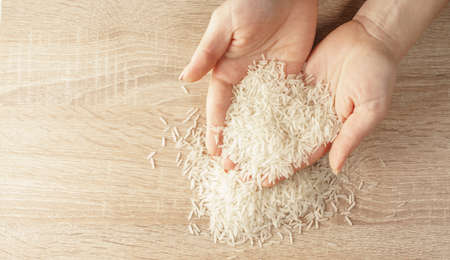 raw rice in hands on wooden backgroundの写真素材