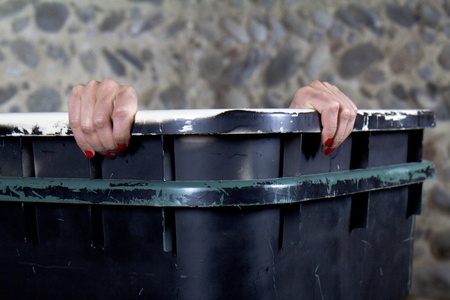 A woman is going to peek out of a garbage container.