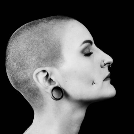 Portrait in profile of a beautiful woman. She shaved her head and she has closed eyes. She's got piercings and earings.の写真素材