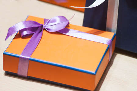 A gift in an orange box with a purple ribbon in a bowの写真素材