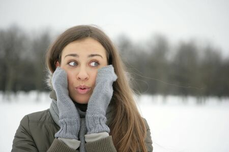 Surprised girl in the park, gloved hands are on her cheeksの写真素材