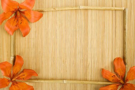 On a wooden surface of the orange flowers tiger lilies and bamboo sticks arranged in a frameの写真素材