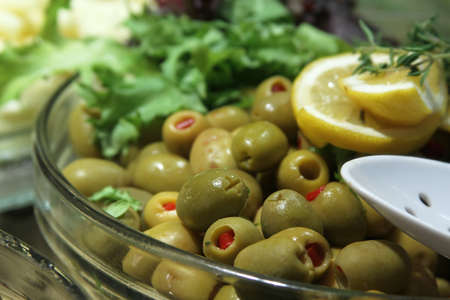 Green olives with lemon and greens on the plateの写真素材
