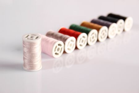 Many multi-colored spools of thread lie in a row. Items on a white background