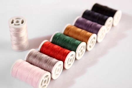 Many multi-colored spools of thread lie in a row. Items on a white background