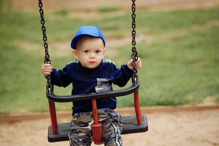 Funny and handsome boy rejoices, rides on a childrens swing, plays on the playground, 1-2 yearsの写真素材