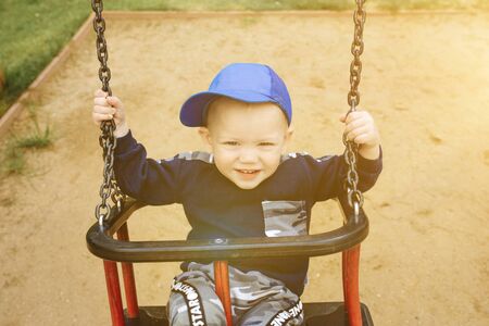 Funny and handsome boy rejoices, rides on a childrens swing, plays on the playground, 1-2 yearsの写真素材