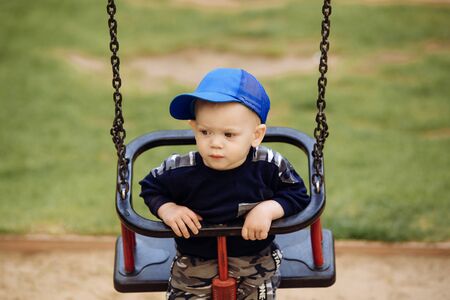 Funny and handsome boy rejoices, rides on a childrens swing, plays on the playground, 1-2 yearsの写真素材