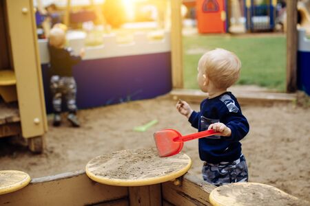 A boy plays in the playground with sand and holds a shovelの写真素材