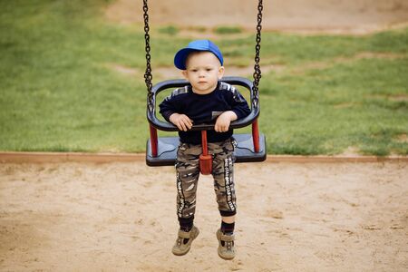 Funny and handsome boy rejoices, rides on a childrens swing, plays on the playground, 1-2 yearsの写真素材