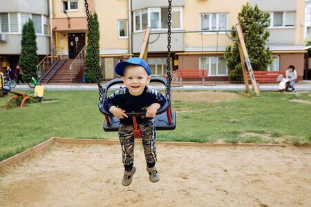 Funny and handsome boy rejoices, rides on a childrens swing, plays on the playgroundの写真素材
