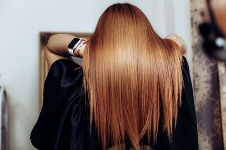 Professional hairdresser shooting straight clients redhead hair after hair care beauty procedures. Back view.の写真素材