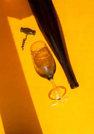 filled glass with water drops, dark glass wine bottle and corkscrew on a bright yellow background in natural light with sharp shadows, vertical image, summer bar menuの写真素材