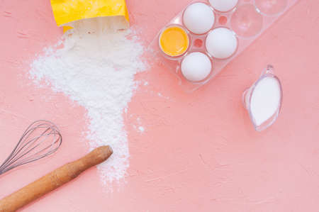 white eggs, a wooden rolling pin, a metal whisk and scattered flour from a yellow bag on a delicate...
