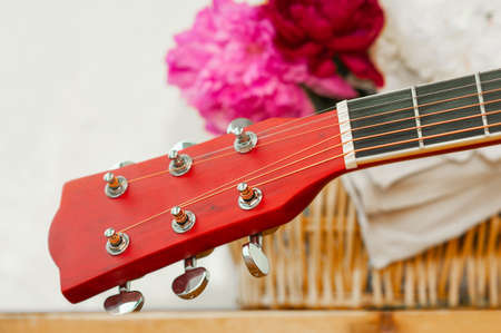 brown fretboard of a six string wooden guitar and blurred multicolored peonies in a wicker basket in the backgroundの写真素材