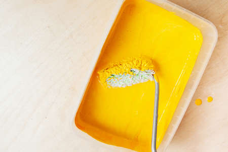 roller collects a bright yellow paint before painting from a transparent form on the plywood...