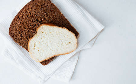 two slices of bread white and black on a white cotton napkin on a white table, top view