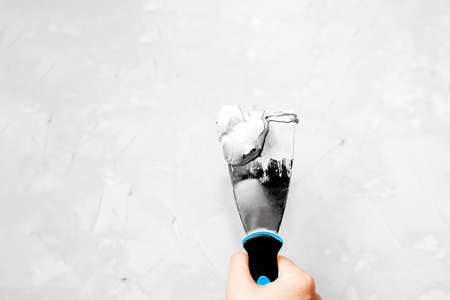 metal spatula with putty or paint with a black handle and a blue stripe in a light skinned hand...