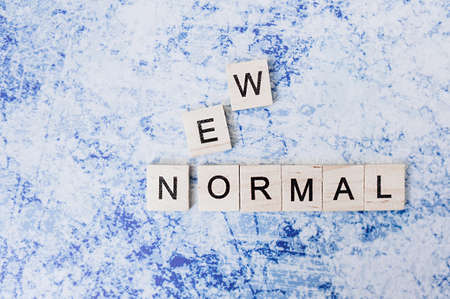 inscription made of small wooden cubes in block letters new normal on a gray-blue cement backgroundの写真素材