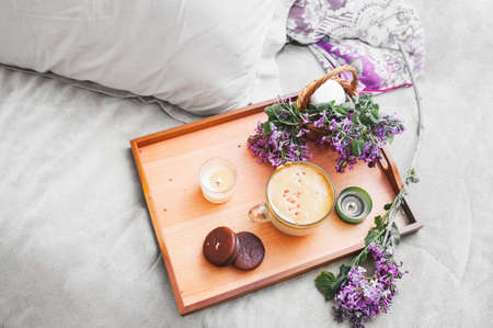 wooden tray with dalgona coffee, chocolate cookies, burning candles and fresh lush purple lilac flowers. cozy beautiful Breakfast in a gray bed with pillows top viewの写真素材