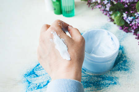 cream on a woman's hand on the background of a large blue jar with a moisturizing and cleansing...